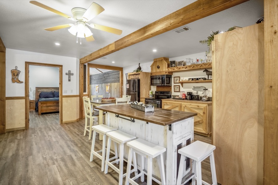 Inspira Ranch barndominium open-plan kitchen with white island, bar stools, and wood beam details — Livingston TX