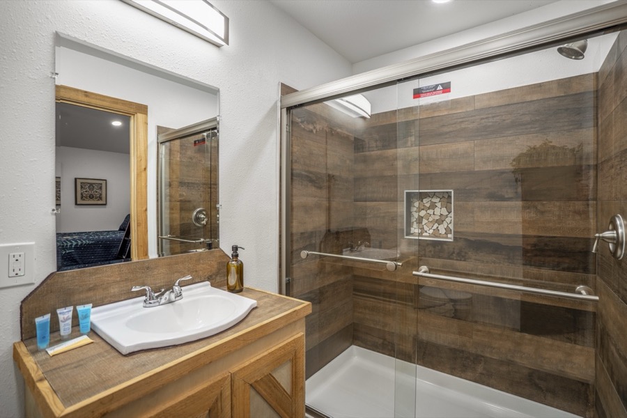 Inspira Ranch barndominium private bathroom with glass-enclosed shower and wood-tone vanity — Livingston TX